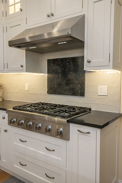 Modern kitchen stainless steel gas stove and range hood with black stone backsplash accent