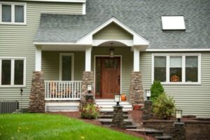 Exterior of house with sage green siding and front porch with stone wrapped columns