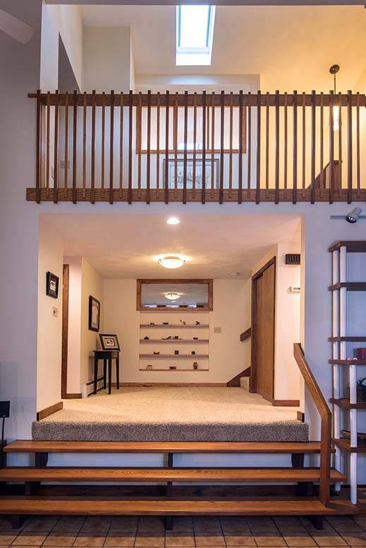 Second-story loft/balcony with rustic wooden railing above carpeted entryway and wooden stairs