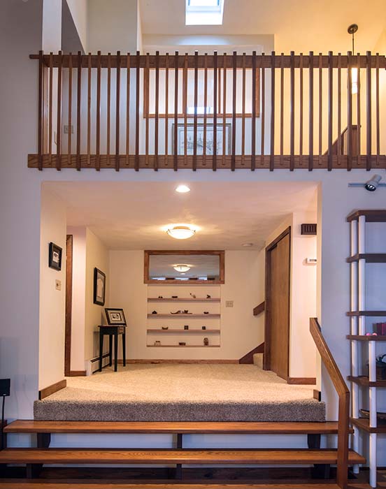 Second-story loft/balcony with rustic wooden railing above carpeted entryway and wooden stairs