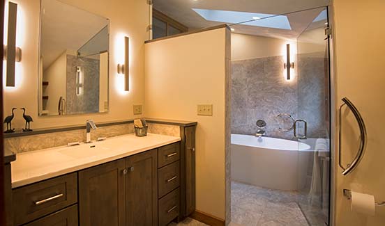 Modern bathroom with grey-tiled tub/shower combo, dark wooden vanity, and metal rod light fixtures