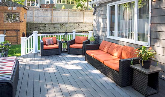Shaded backyard deck with black wicker furniture and orange cushions
