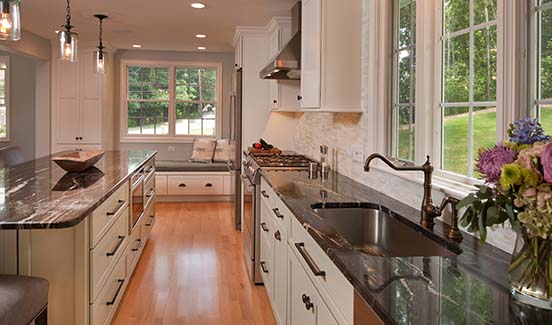 Kitchen remodel with black marbled countertops, off-white cabinetry with black hardware, and a window bench