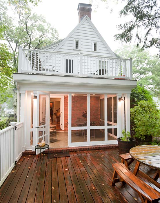 White four seasons/screened porch addition against red brick house exterior, leading onto back deck