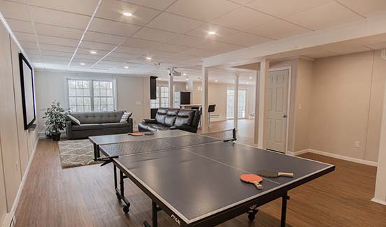 Bright open-plan basement remodel with leather couches, ping pong table, and projector screen