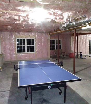 Unfinished basement with pink insulation and a ping pong table