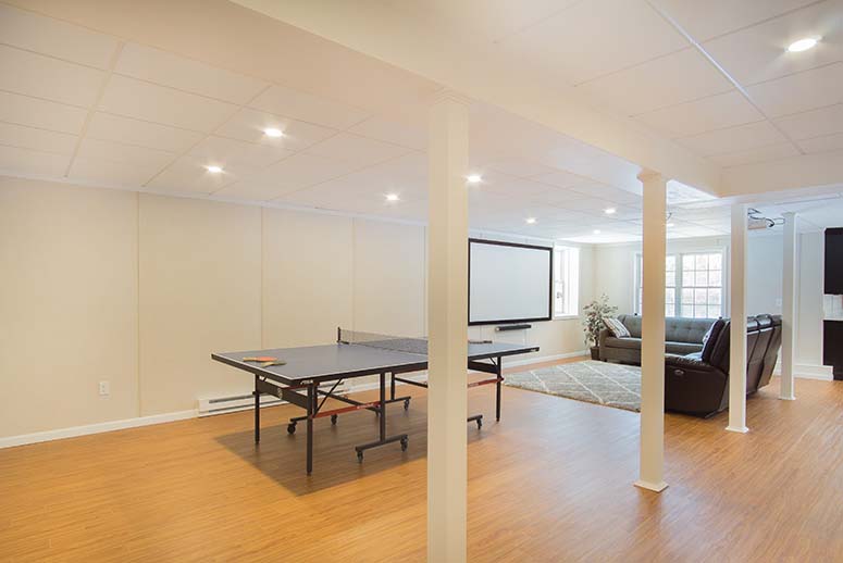 Bright open-plan basement remodel with leather couches, ping pong table, and projector screen