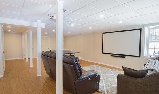Bright open-plan basement remodel with leather couches, ping pong table, and projector screen