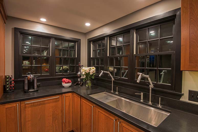 Remodeled kitchen with cherry wood cabinets and black stone countertops and window trim on two rows of double-hung windows with grids.