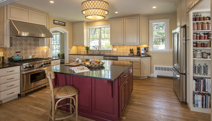 Large remodeled kitchen with wood floors, dark stone countertops, red cabinets for island, white cabinets against wall.
