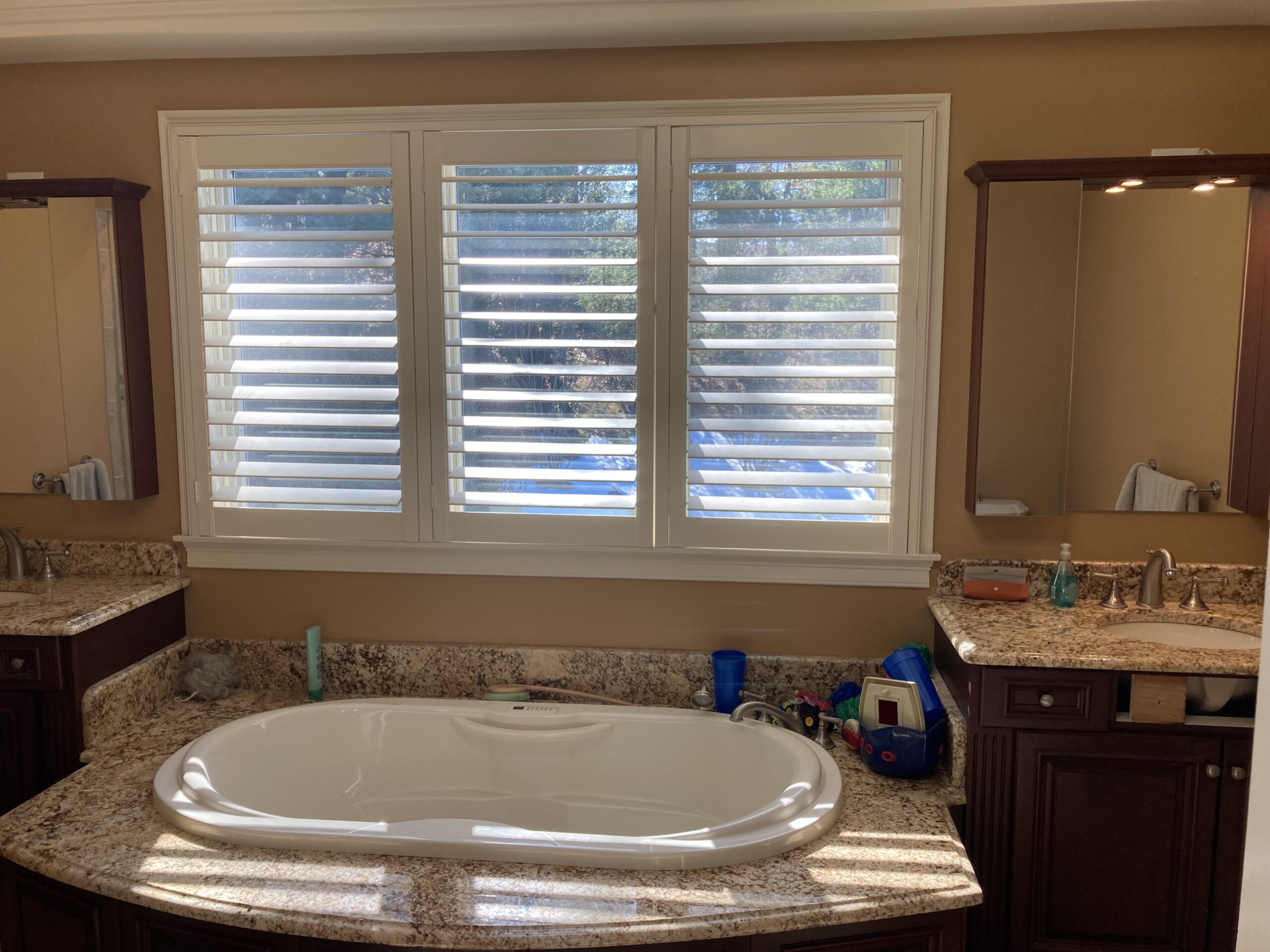 Bathtub under window with brown,wooden sinks on both sides