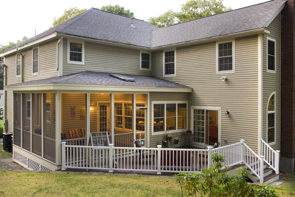 Screened in porch connecting to a back deck on a large two-story tan home.