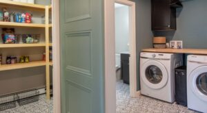 Modern designed laundry room next to pantry. Tile flooring, light blue door, open wood shelving.