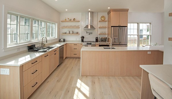 Minimalist Kitchen Remodel with Scandinavian design. Light wood floors and cabinets, white stone countertops, long row of windows over the counter, open shelving on far wall, large island with waterfall countertop.