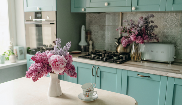 Remodeled kitchen with robin's egg blue cabinets in background and pink and purple lilacs in white vase on white island countertop in foreground.